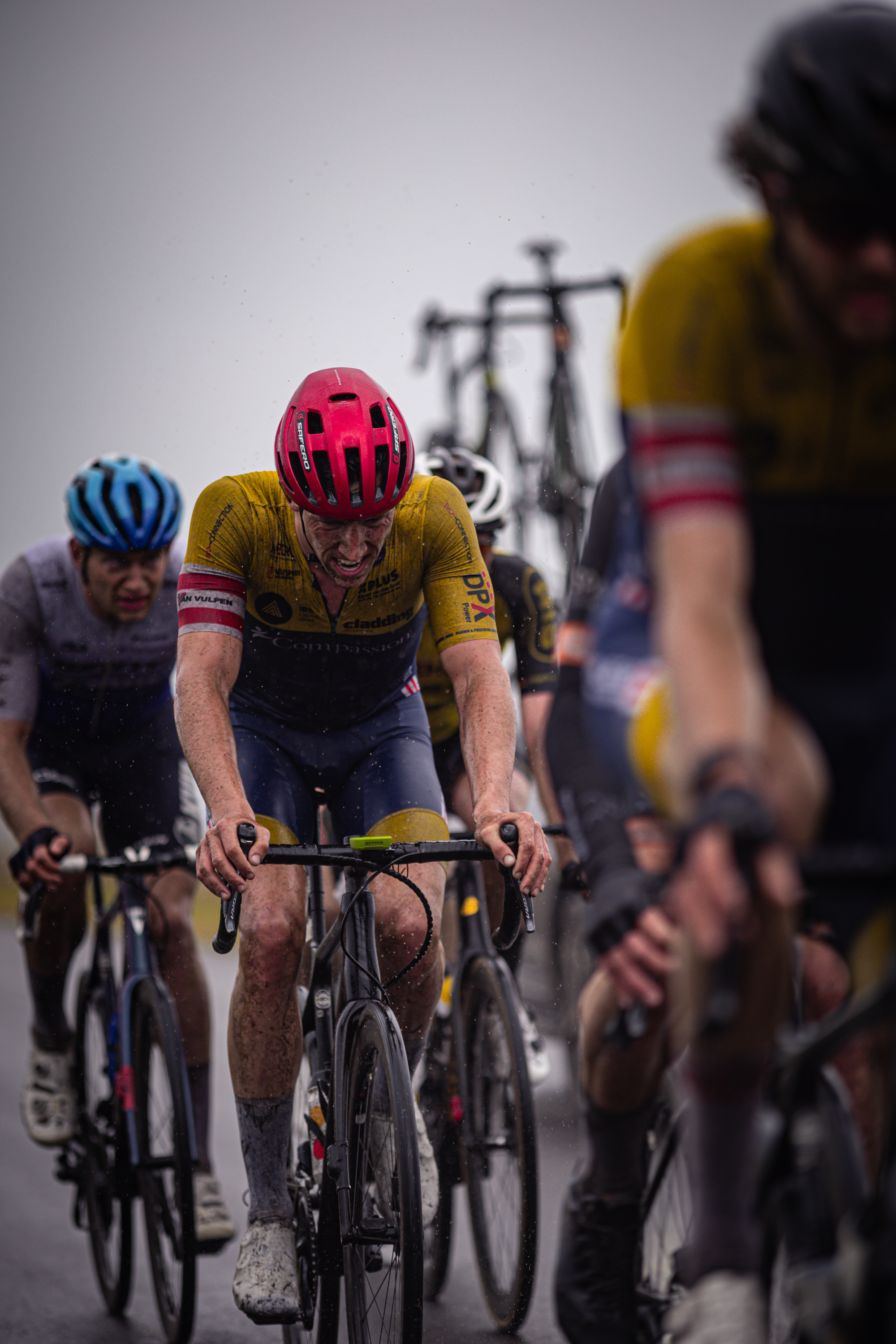 A cyclist wearing a red helmet is riding a bike with other cyclists in the background.