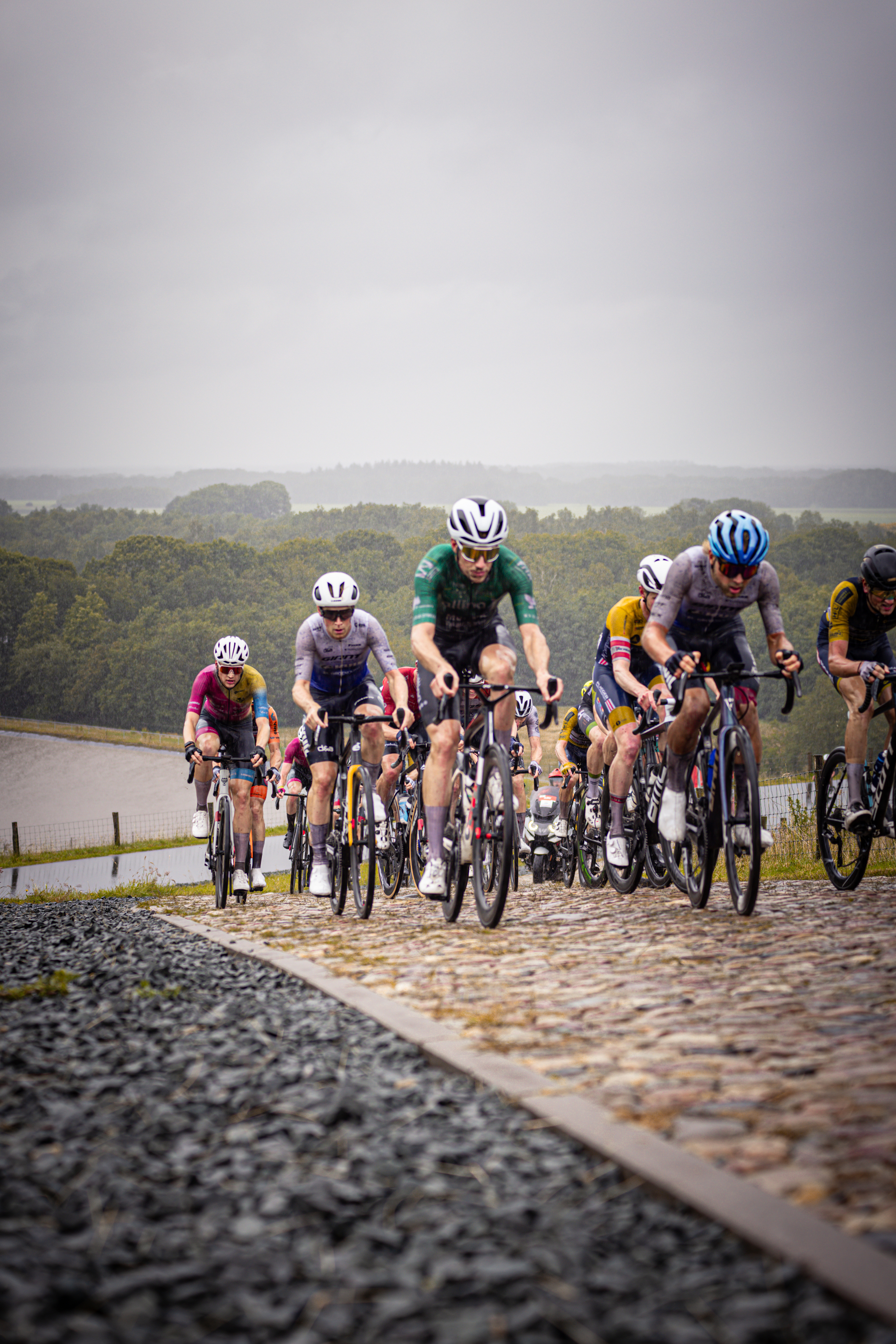 A group of cyclists riding on a cobblestone road with one wearing the number 18.