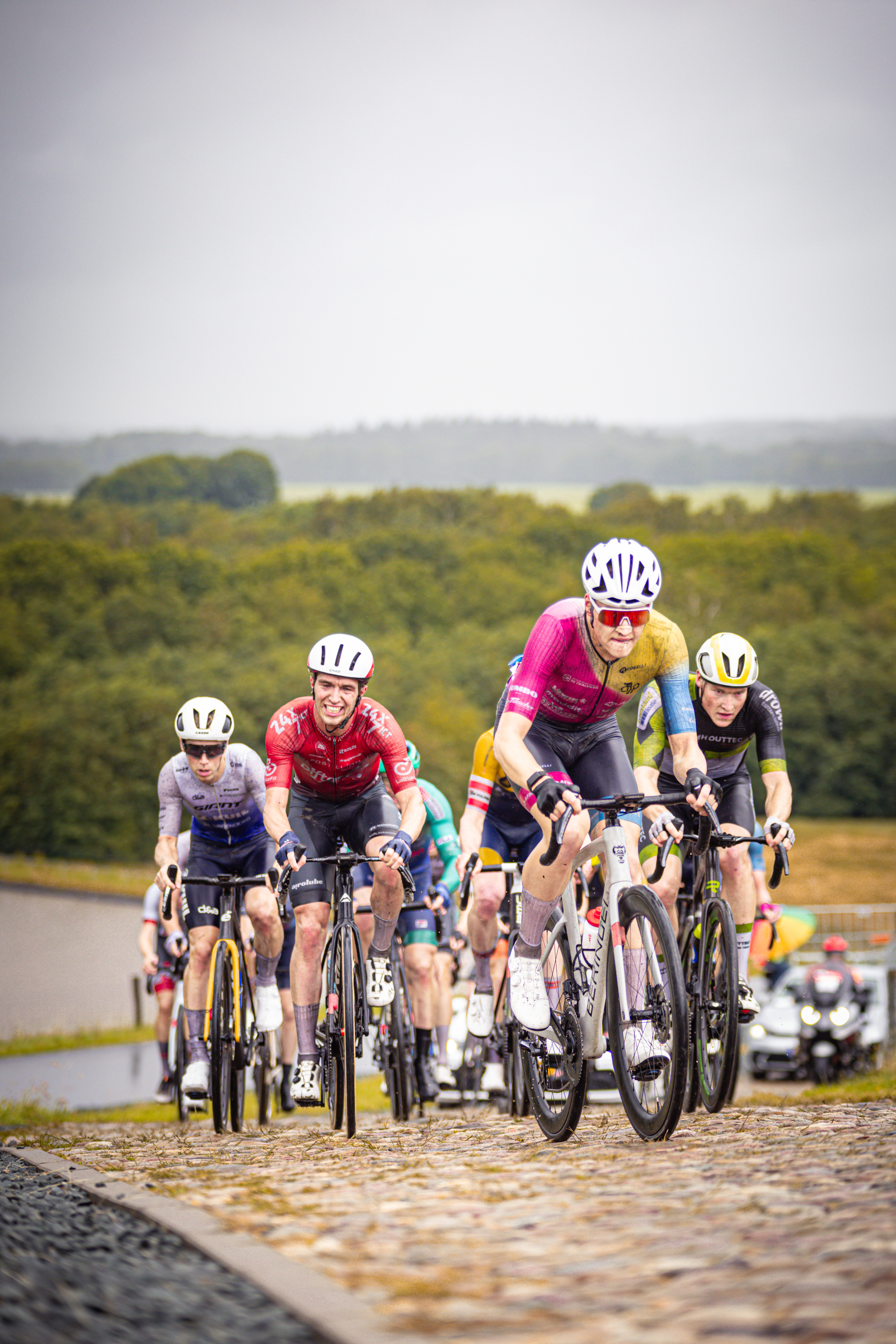 A group of cyclists wearing helmets and riding bikes on a cobblestone road.