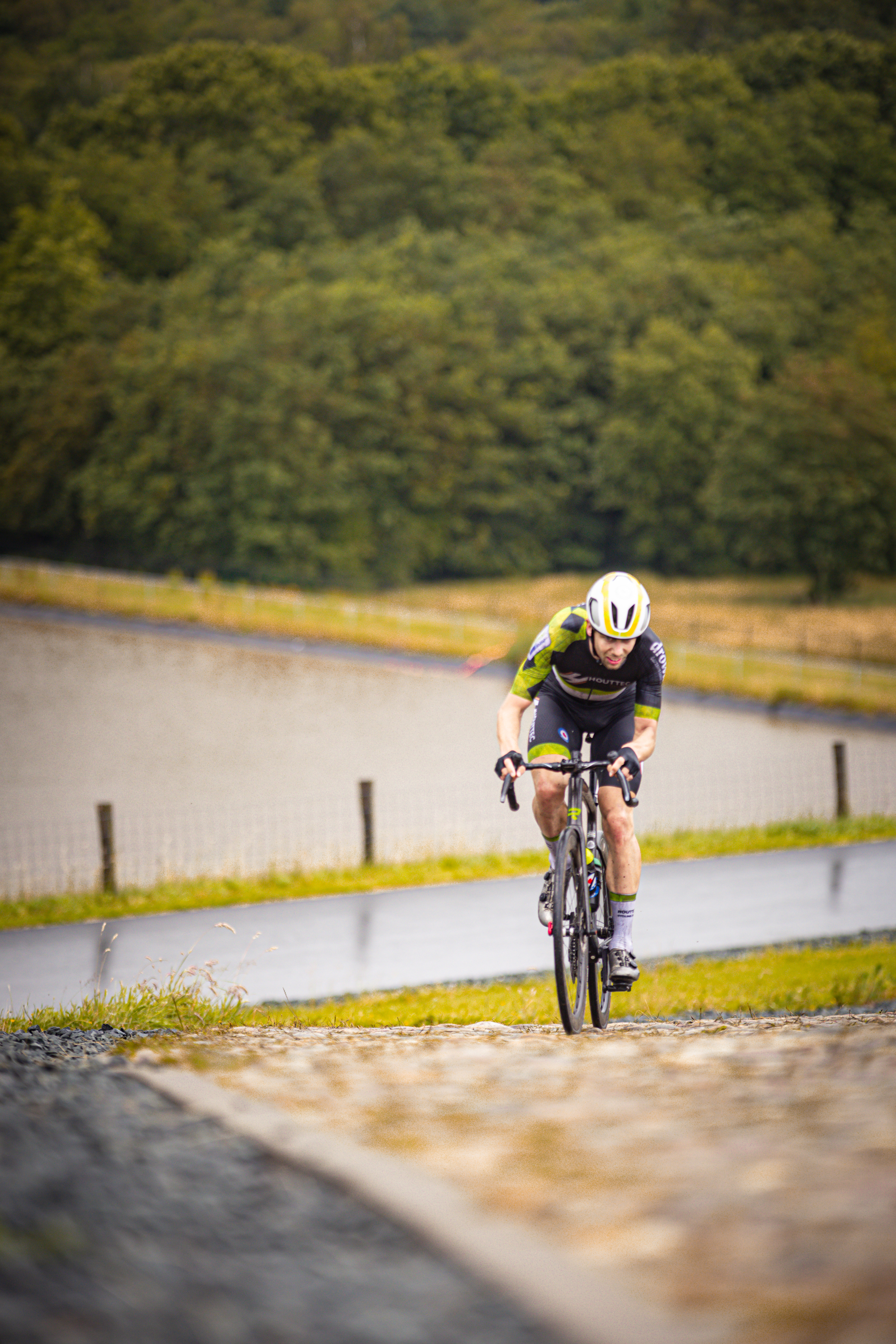 A cyclist in a yellow helmet is racing on the cobblestones of a riverbank.