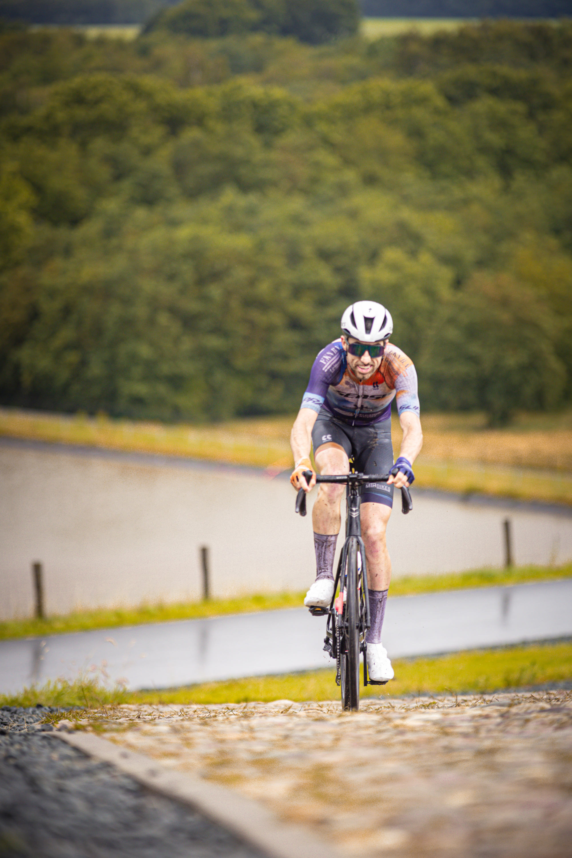 A man wearing a helmet and jersey, riding a bike with 2 hands on the handlebars. He is going up a hill.