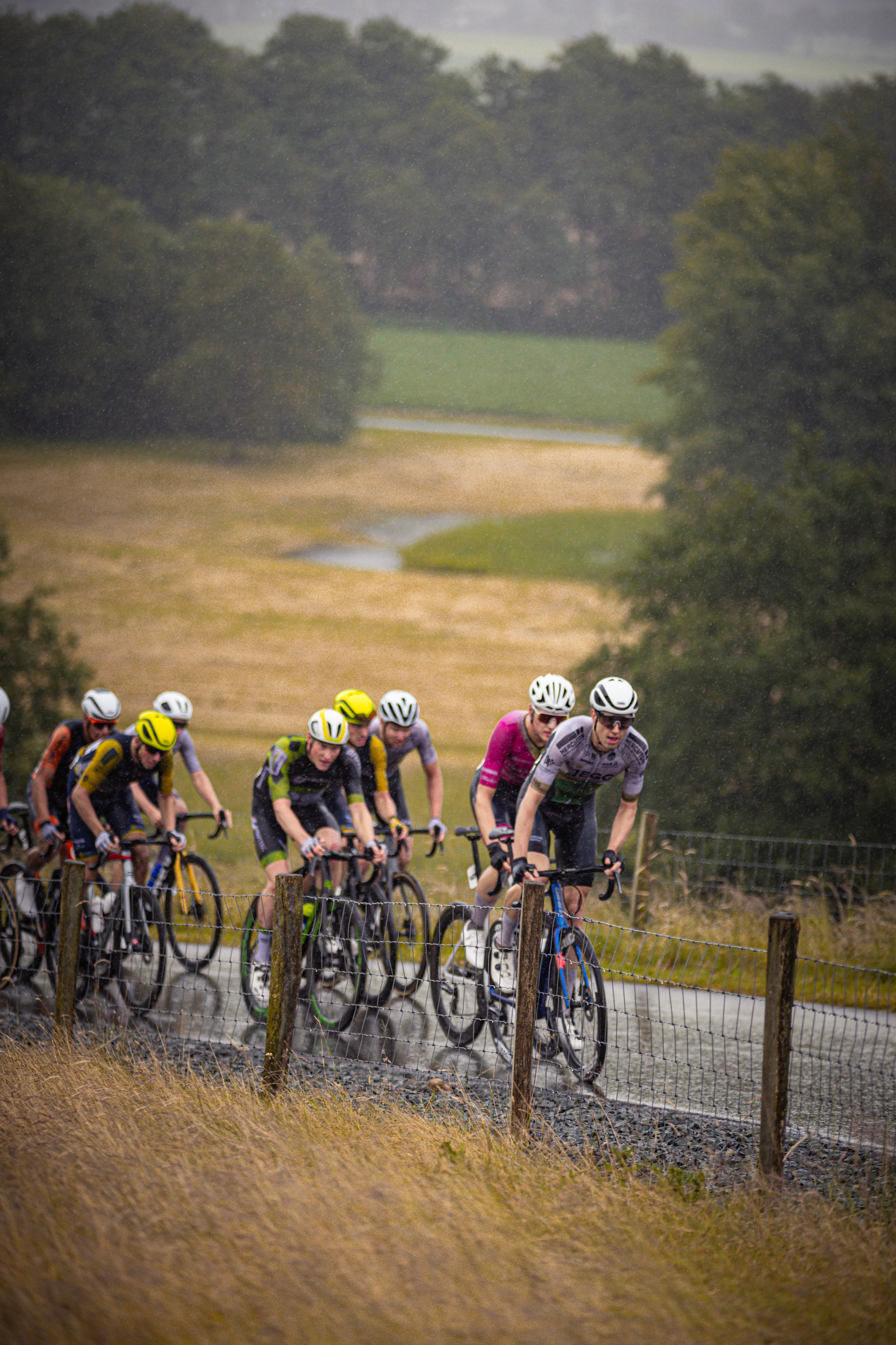 The cyclists are riding on a hill and the person in the middle is wearing a yellow helmet.