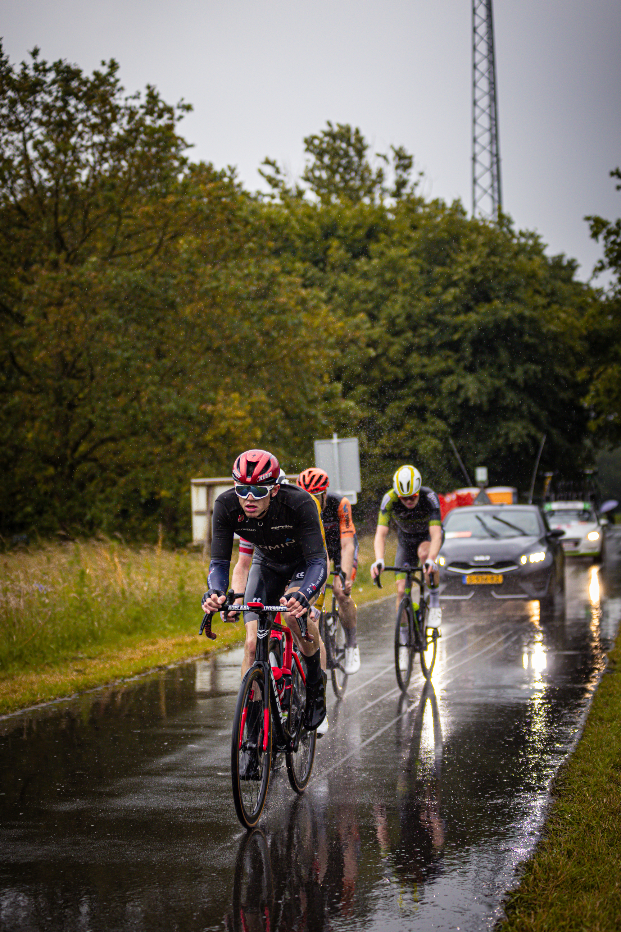 A group of bikers race through a street that's wet from rain.