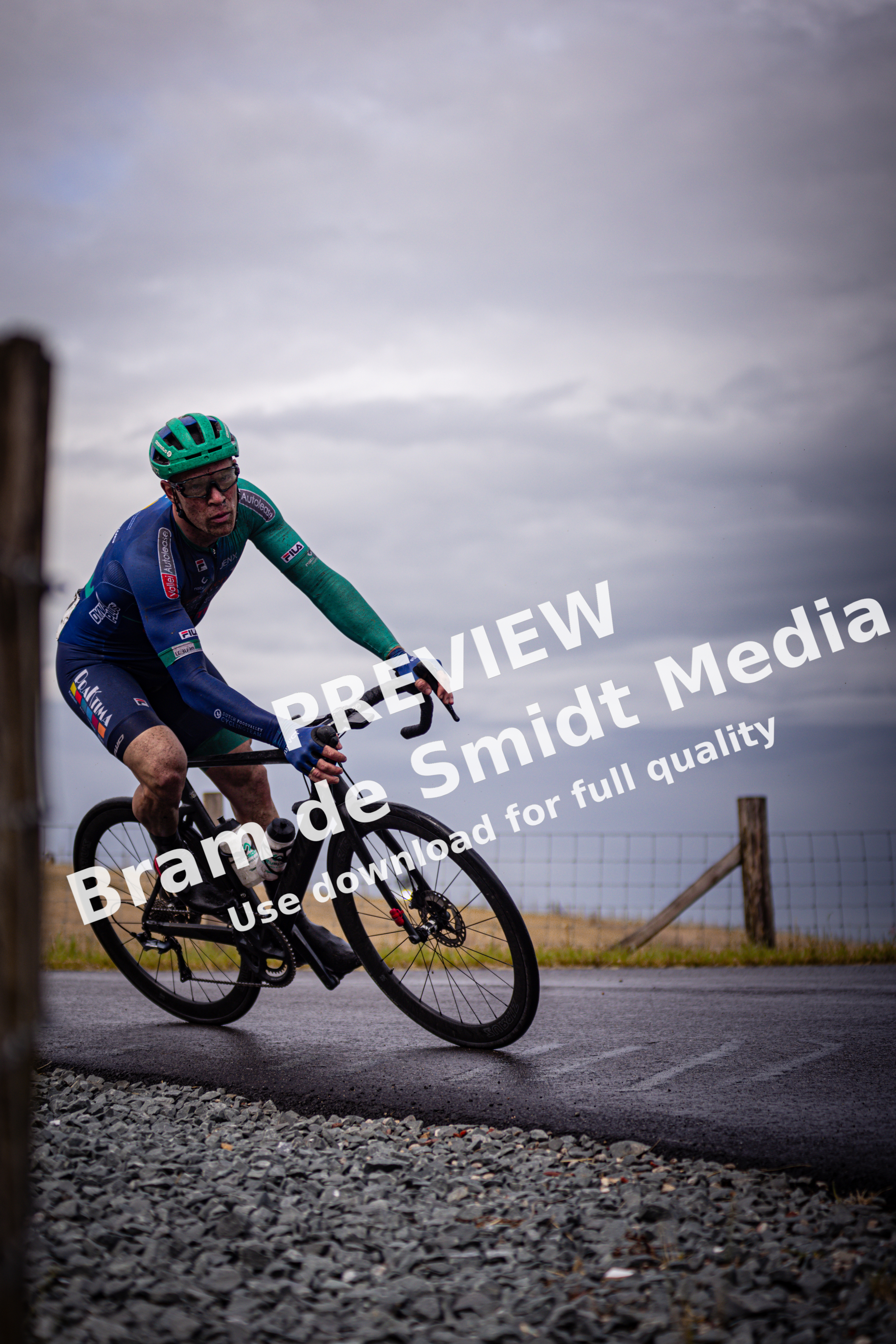 A man on a bicycle wearing a blue, green and black uniform with the word "Wielrennen" on it.