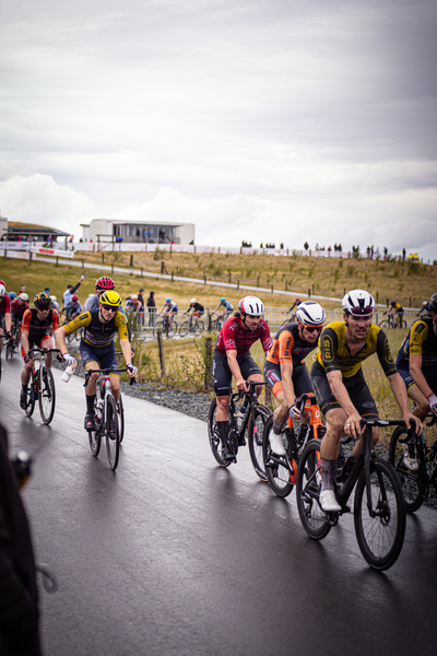 A group of racers are riding along a wet road on the Nederlands Kampioenschap, Wielrennen Mannen Elite ZC.