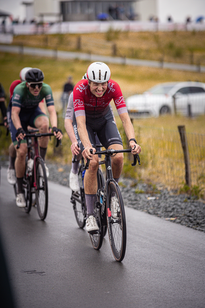 Two cyclists on a road, one with an  N on his shirt, both wearing helmets and riding black bikes.