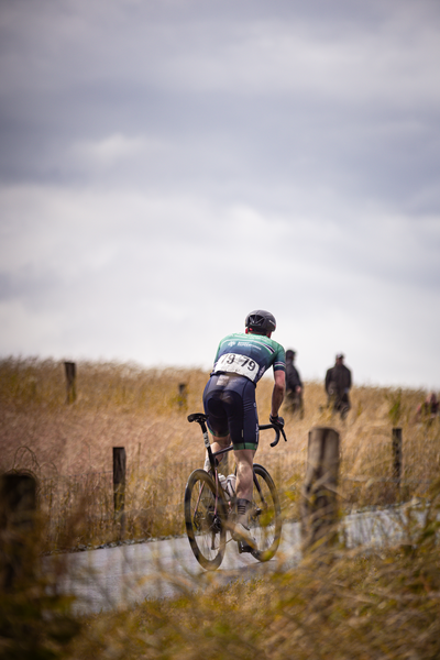 A man in a black and green cycling uniform on a bike on a dirt road.