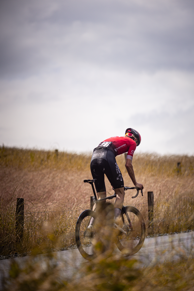 A man is riding a bike, wearing a red shirt with the word "Wielrennen" on it and black shorts.