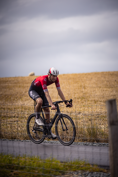 A man wearing a white helmet and a red jersey is riding a black bike on a road.