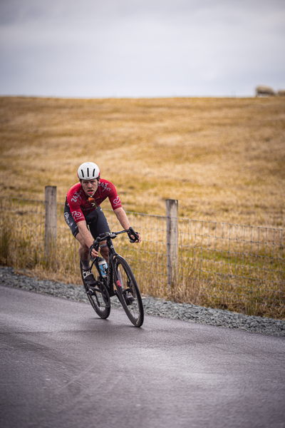 A cyclist wearing a red and black jersey, with the number 4 on it, on a road.