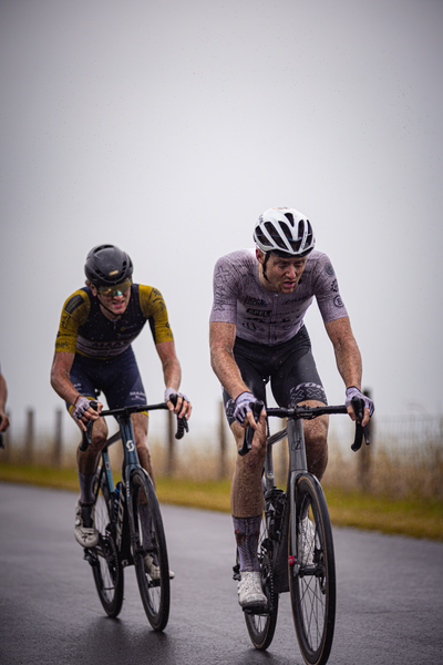 Two cyclists race down a road with Nederlands Kampioenschap Wielrennen Mannen Elite ZC written on their jerseys.