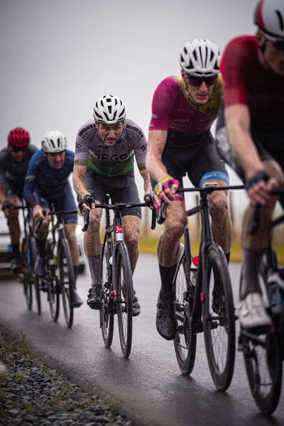 Bikers race on a paved track in the rain during a competition.