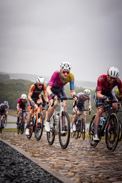 A cyclist wearing a red shirt races down a cobblestone road during the Nederlands Kampioenschap.