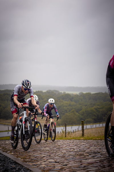 Three bicycle racers on a cobblestone road, racing towards the finish line.