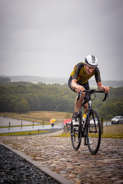 A man wearing a black and yellow shirt is riding his bicycle down a cobblestone road.