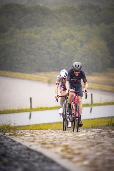 Two cyclists in the rain race each other on a wet cobblestone road.