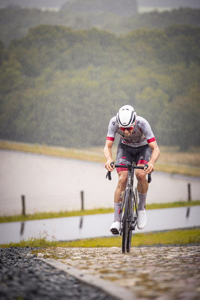 A man on a bike, wearing a white helmet and riding in the rain.