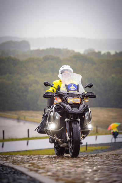 A person wearing a yellow helmet and jacket is riding a motorized bike on an unpaved road.