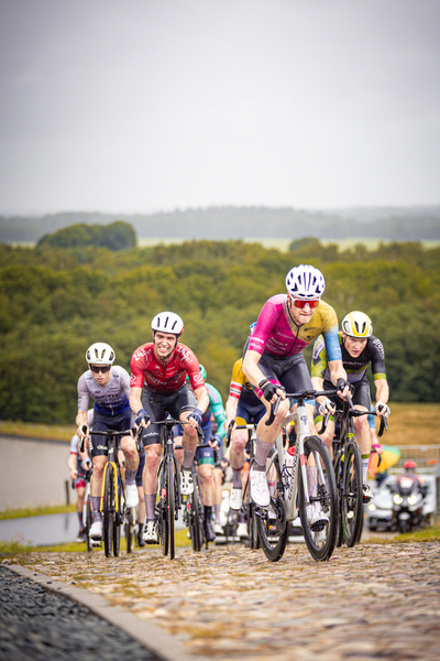 A group of cyclists wearing helmets and riding bikes on a cobblestone road.