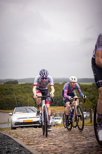 Two men are riding bicycles in a race. One of them is wearing a jersey with a blue, white and red design.