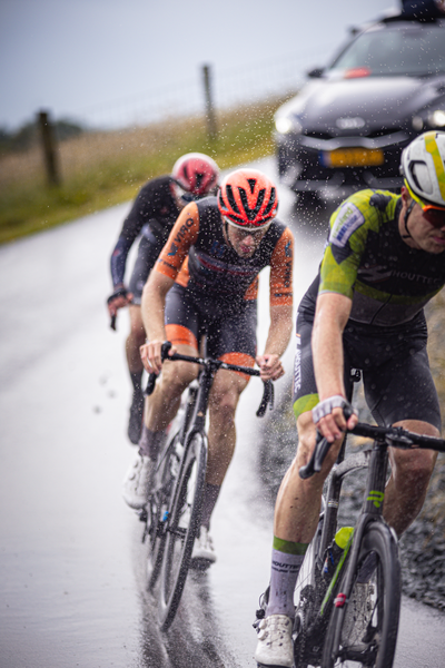 Three cyclists racing on a wet road as they participate in the Nederlands Kampioenschap.