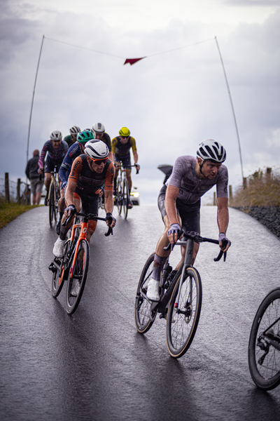 A group of cyclists wearing helmets ride down a road.