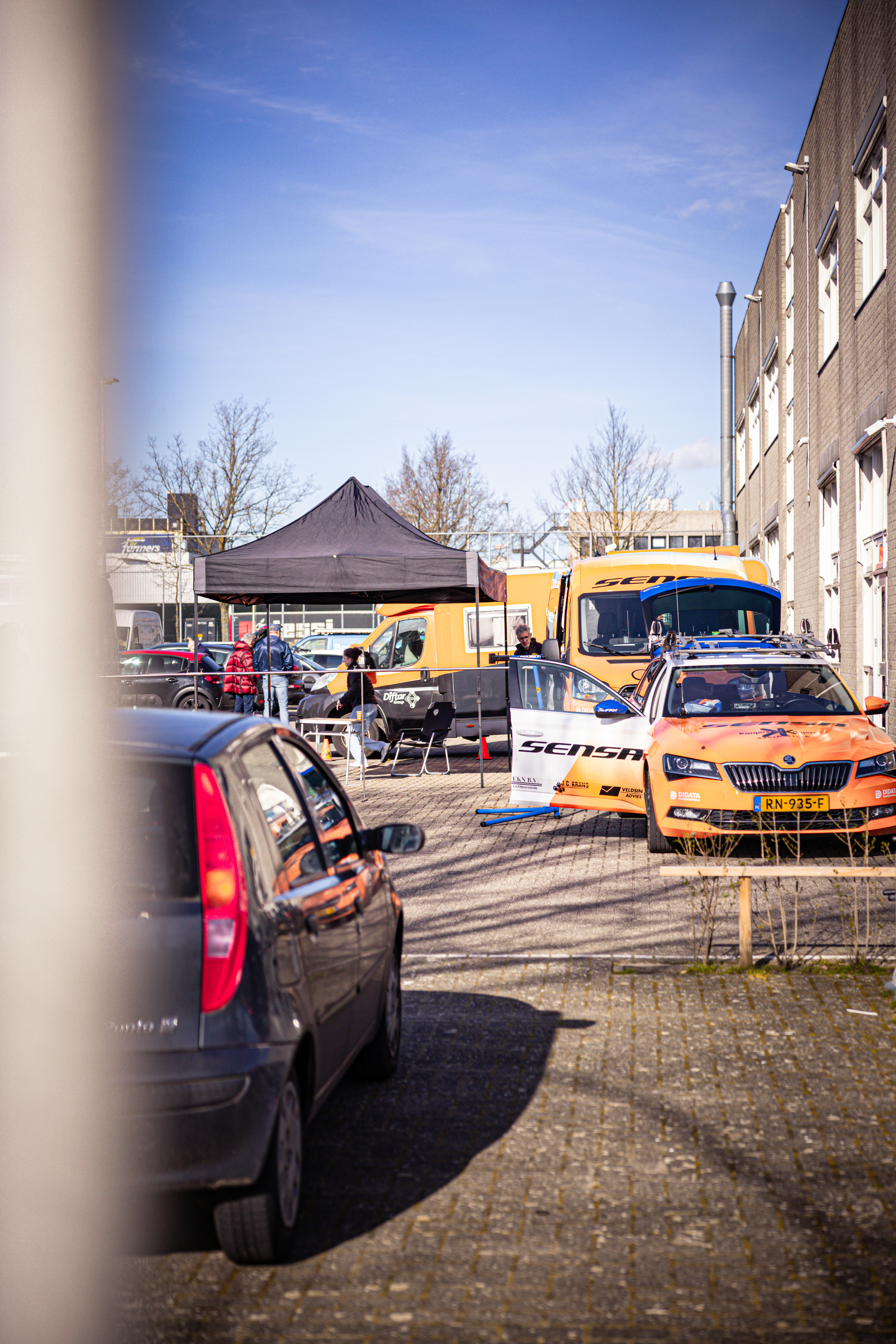 A car with the word "Wielrennen" written on it is parked in front of a building.