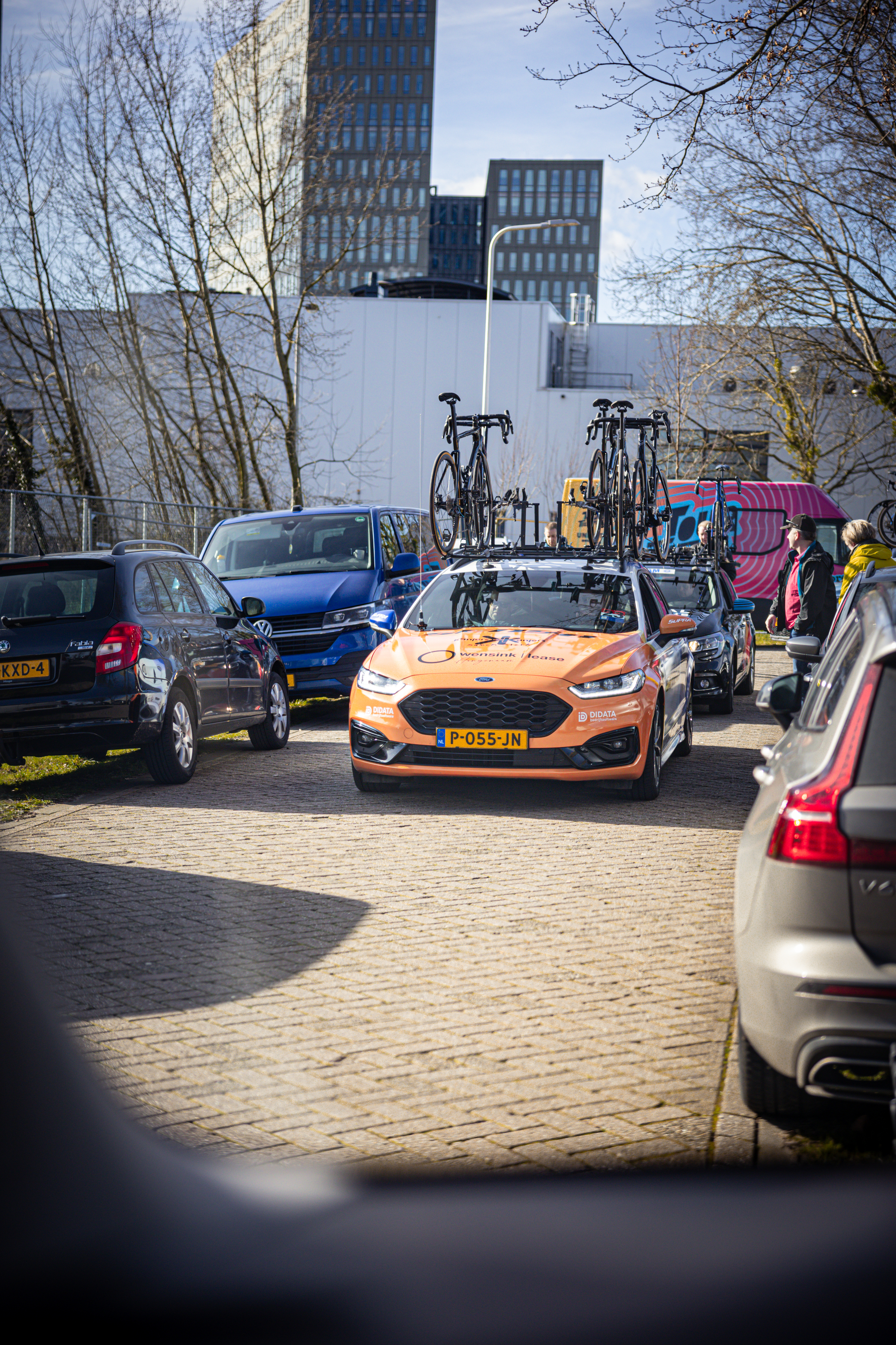 Two orange race cars, one with a blue bicycle on the roof.