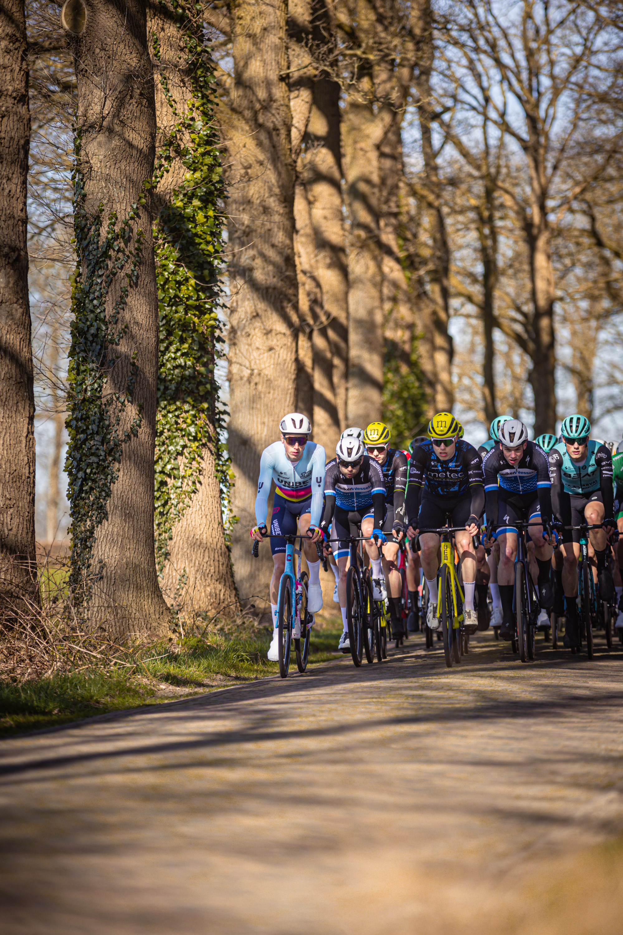 A group of cyclists wearing helmets are riding down a road.