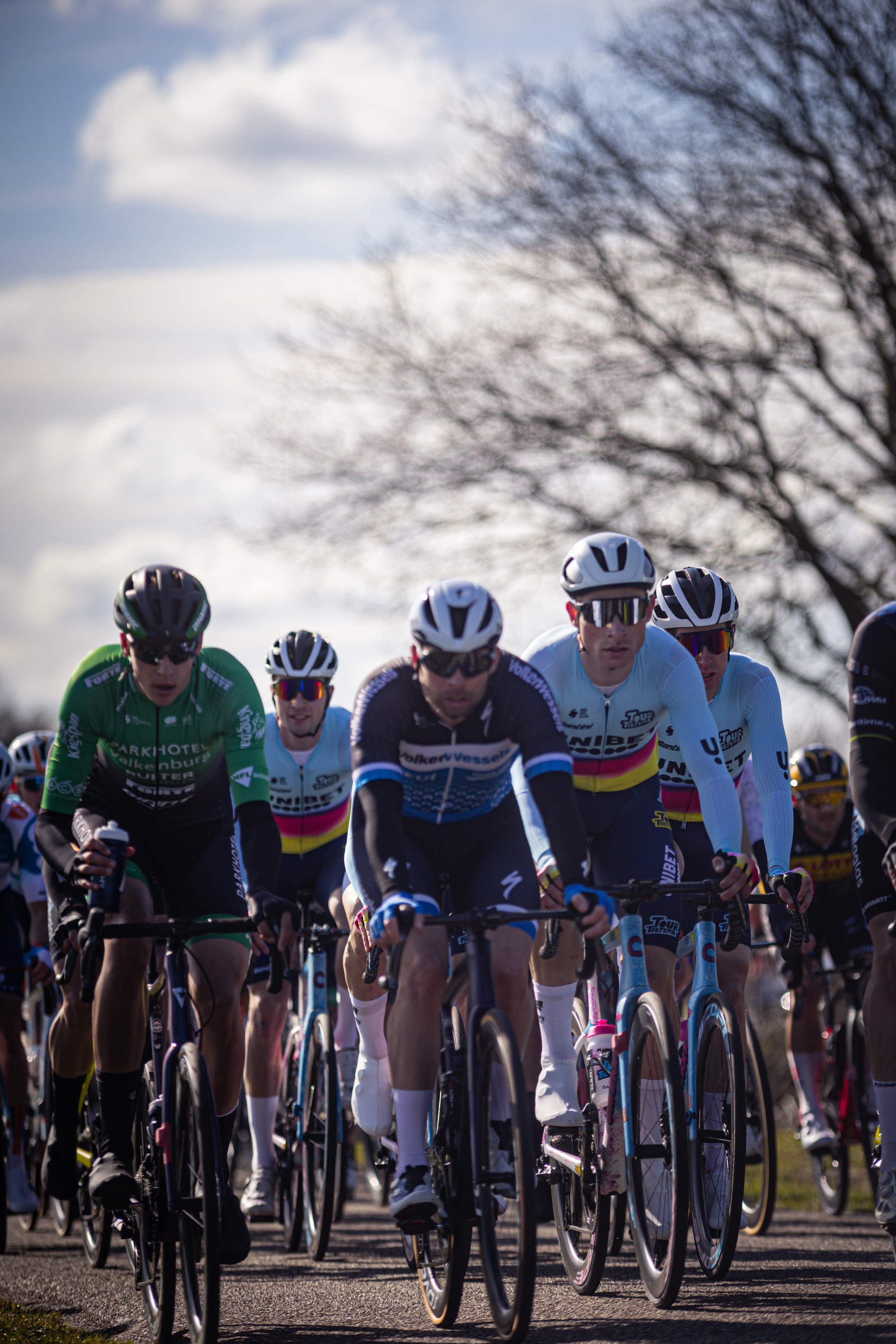 Several cyclists are riding in a group and one is wearing the number 12 on his jersey.