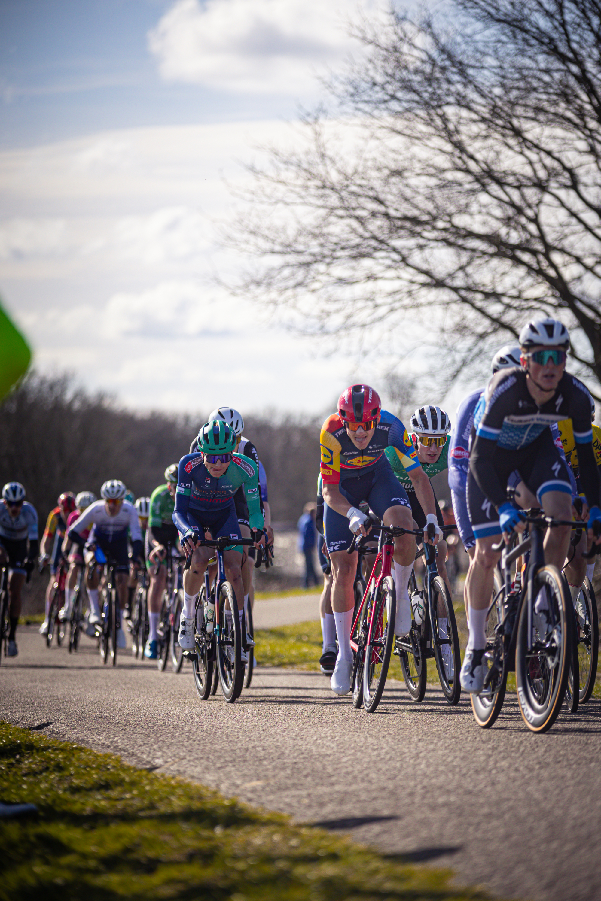 A group of cyclists race down the road, wearing colorful jerseys and helmets.