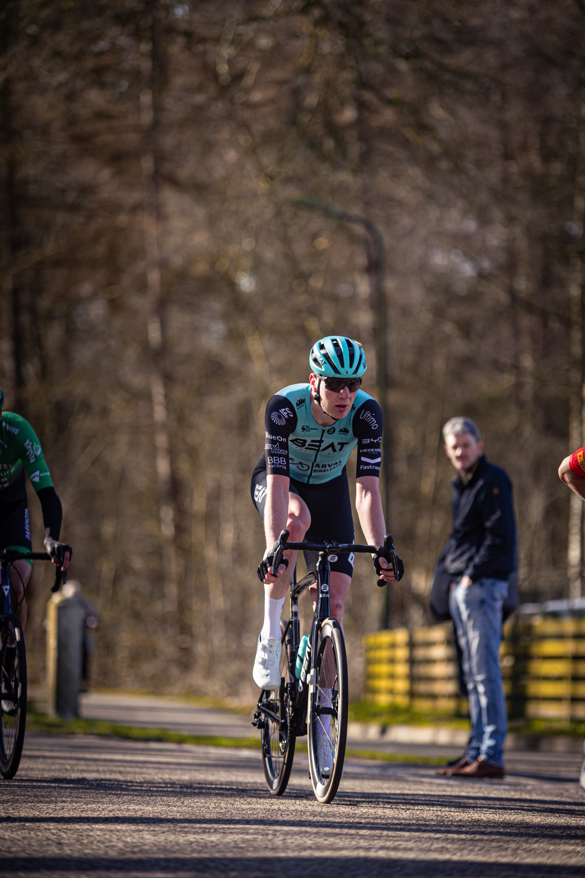 Two cyclists are riding through a forest, one of them wearing a black jersey that says "ster" on it.