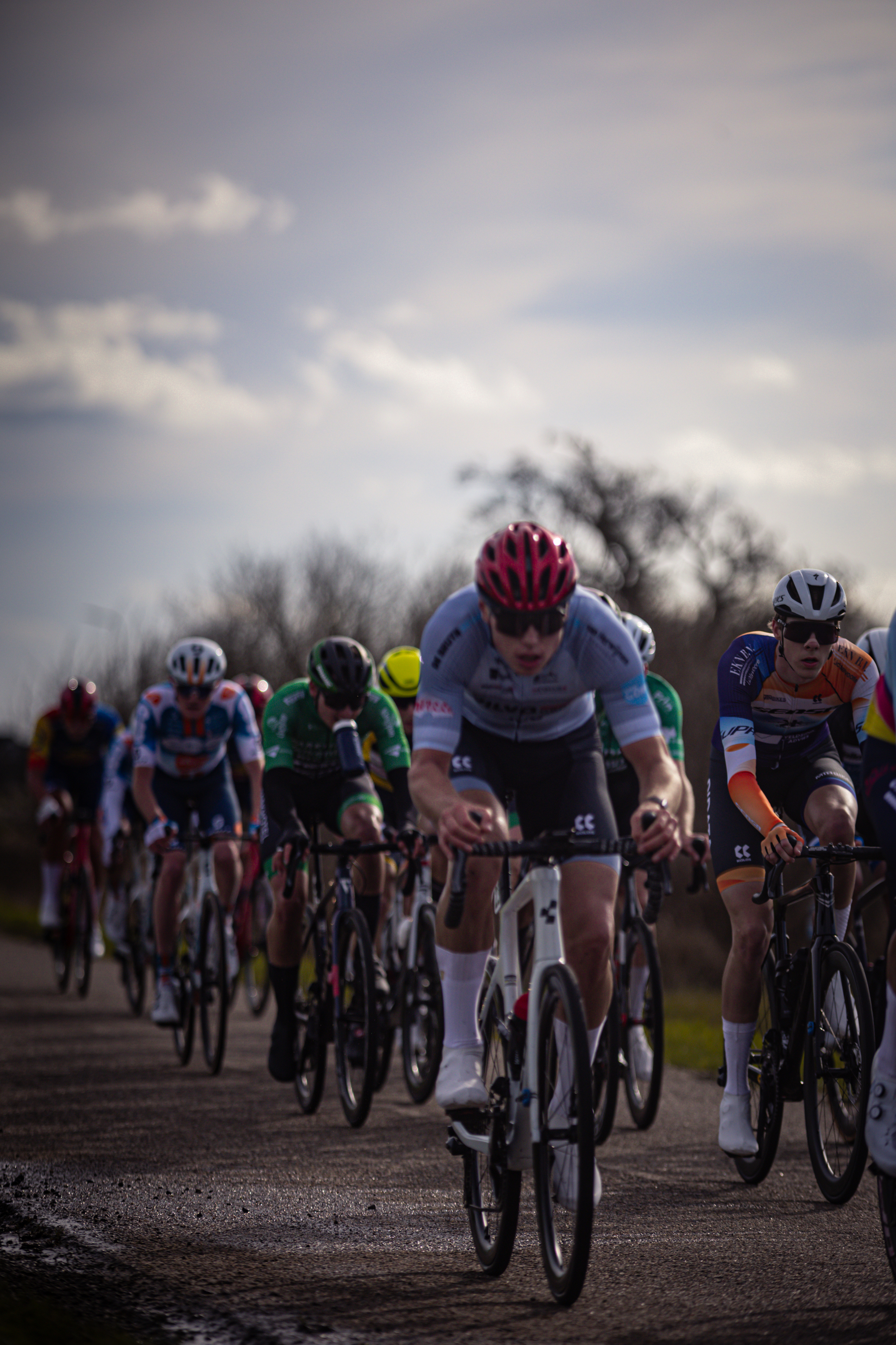 A group of cyclists in a race, one wearing a red helmet and another an orange one.