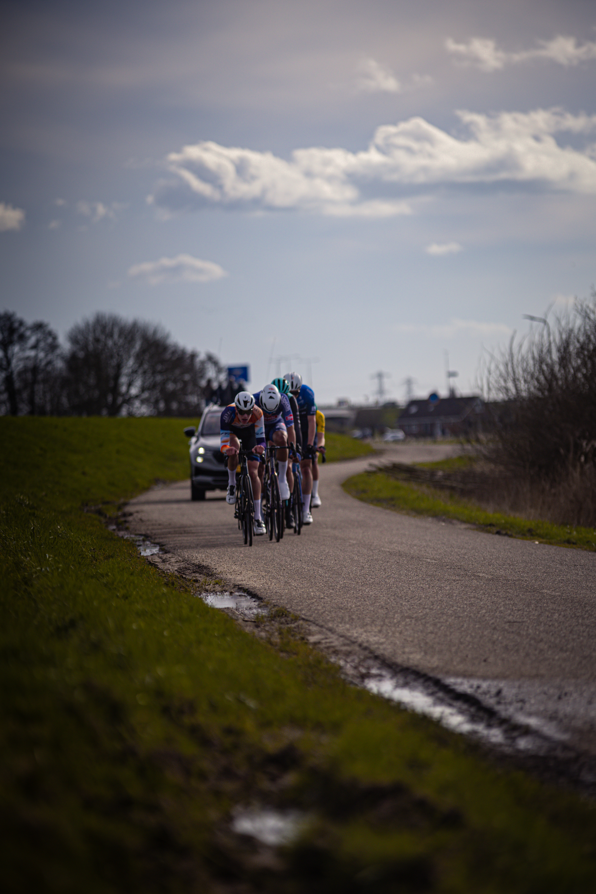 A group of people are riding their bikes down a wet road with the word Wielrennen on it.