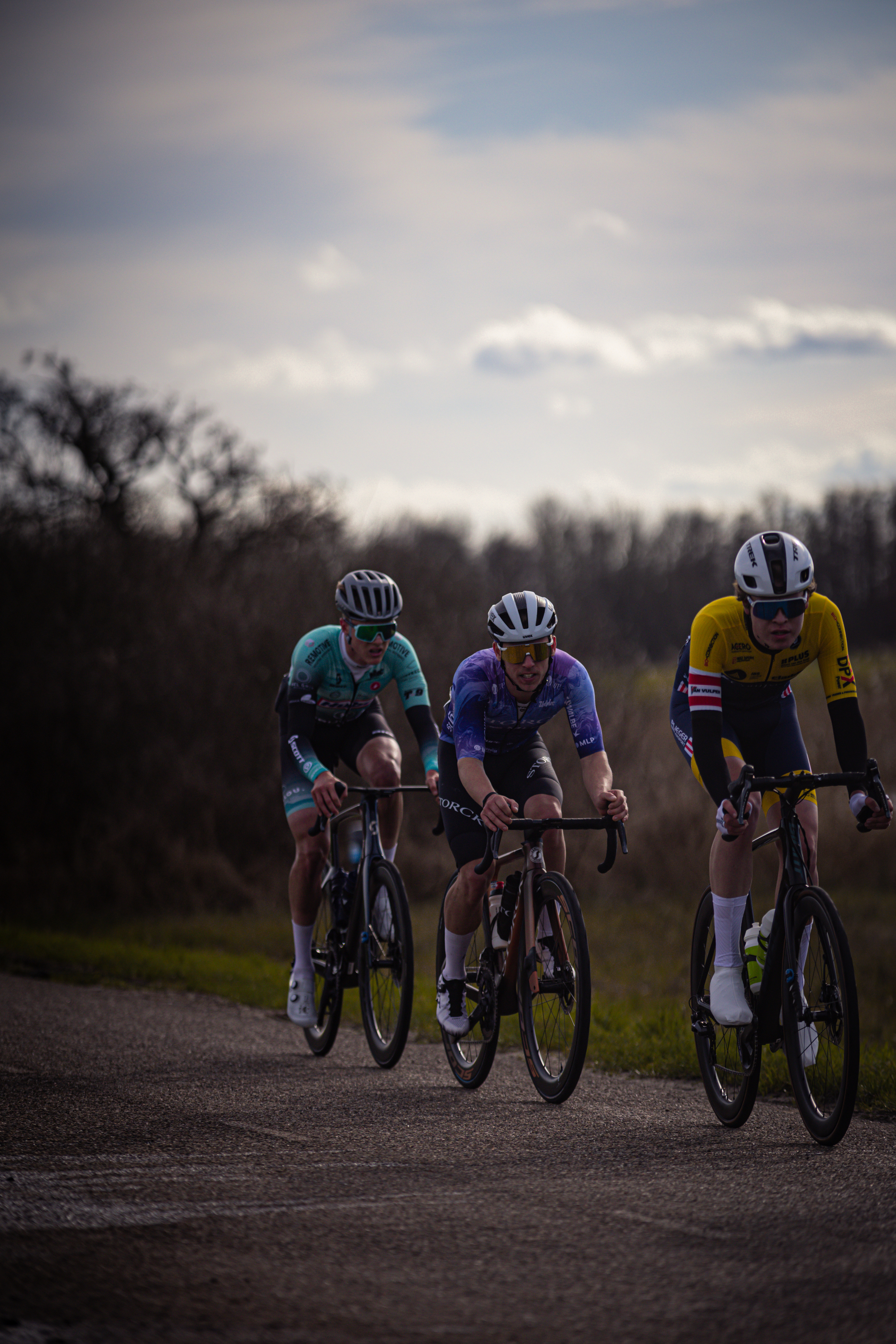 Three cyclists in a race, the second from right is wearing a blue and white jersey that says "Ster van Zwolle".