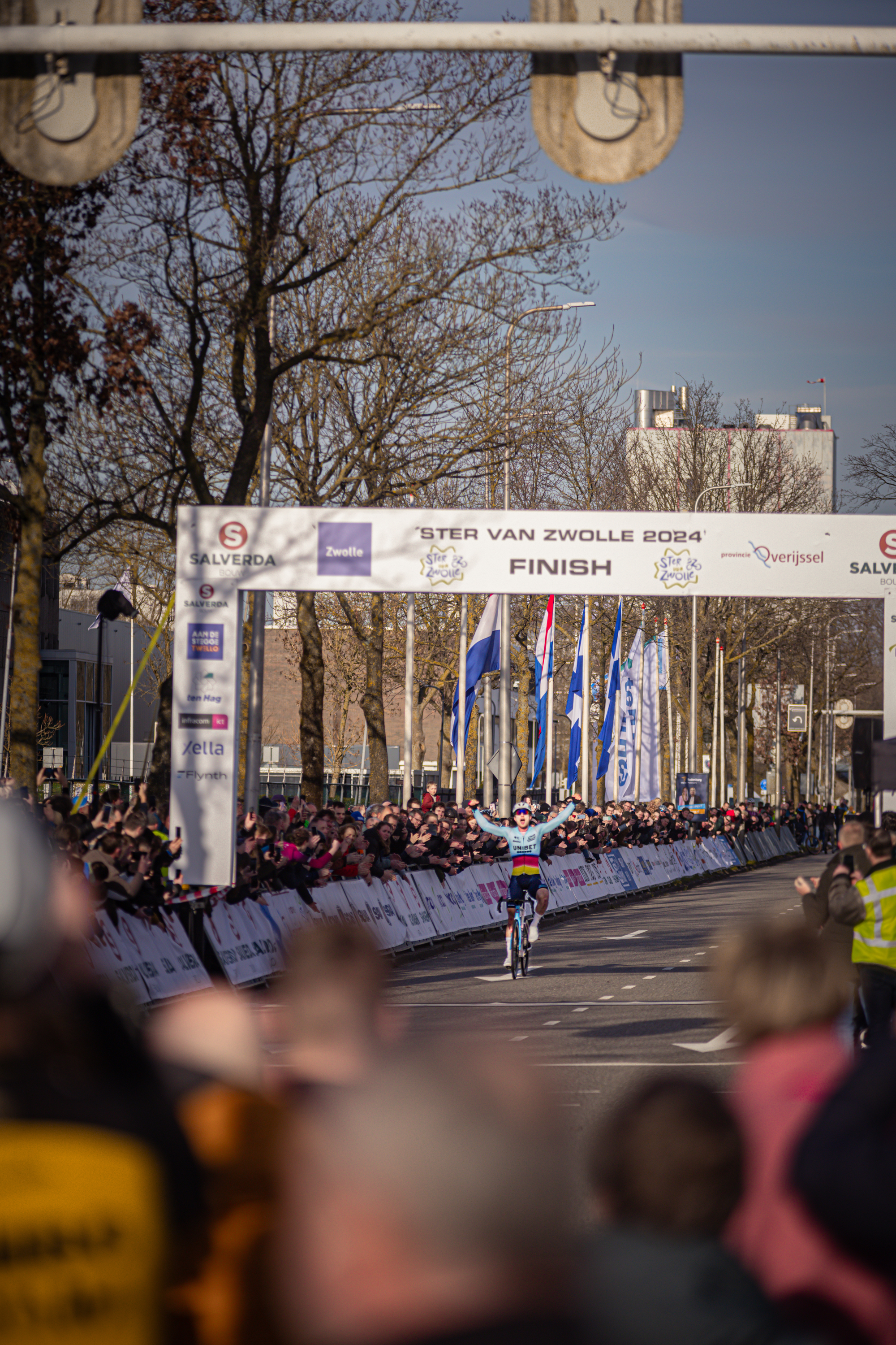 A cyclist in a blue and white jersey is riding through the finish line at Ster Van Zwolle.