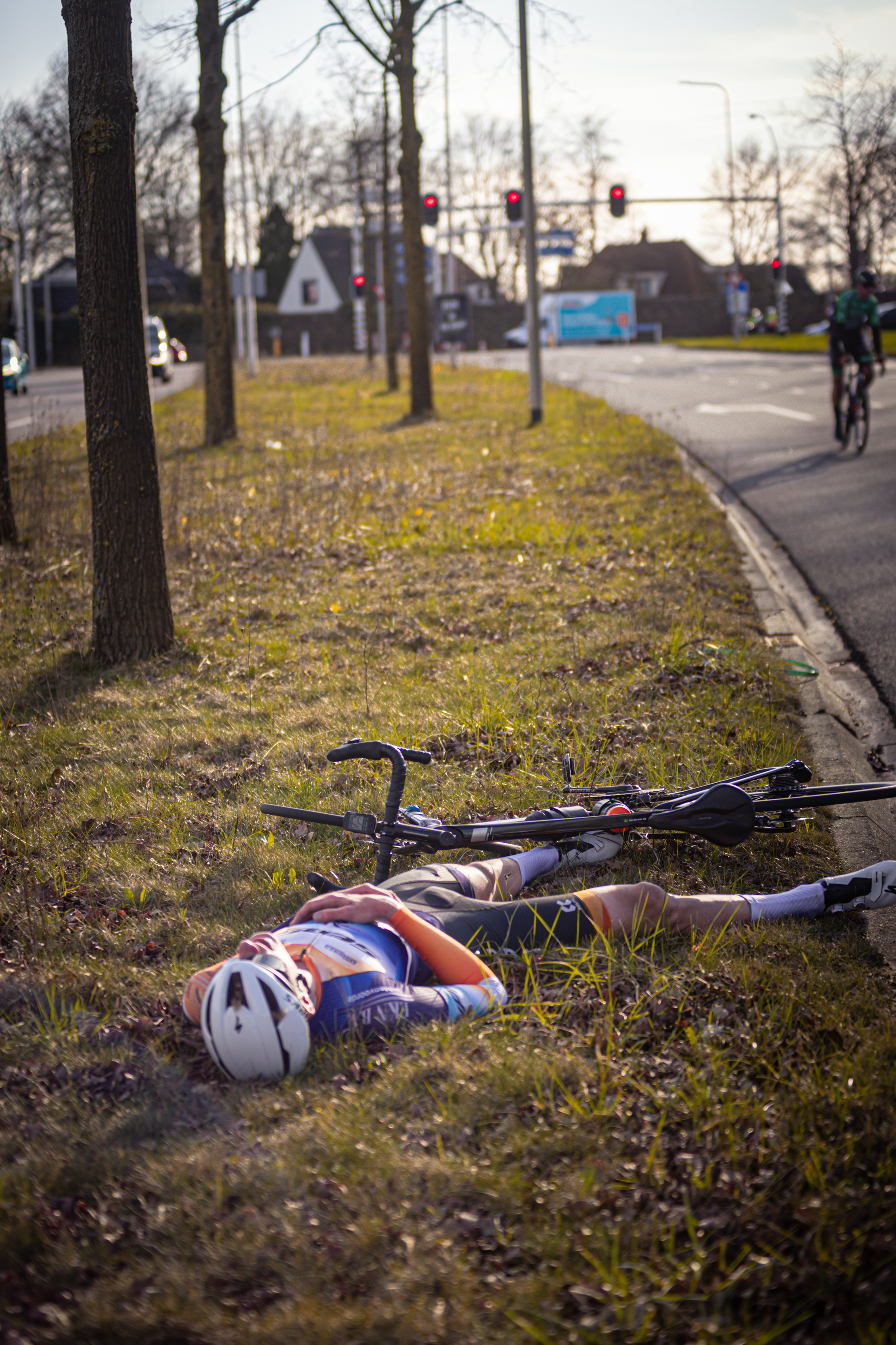 A person is laying down in the grass beside a bicycle, near the side of the road.