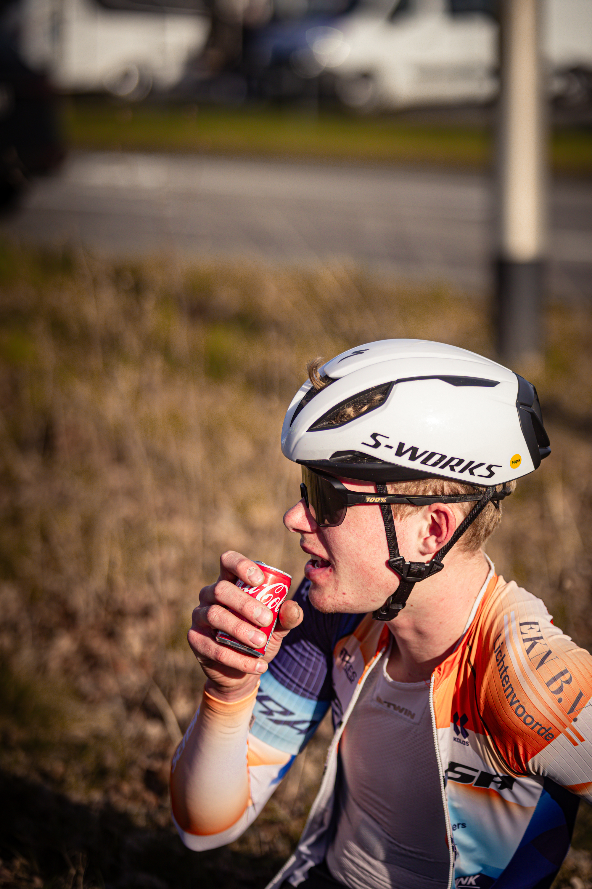 A cyclist is taking a drink of water while wearing a white bike helmet with the brand name S-Wolde on it.