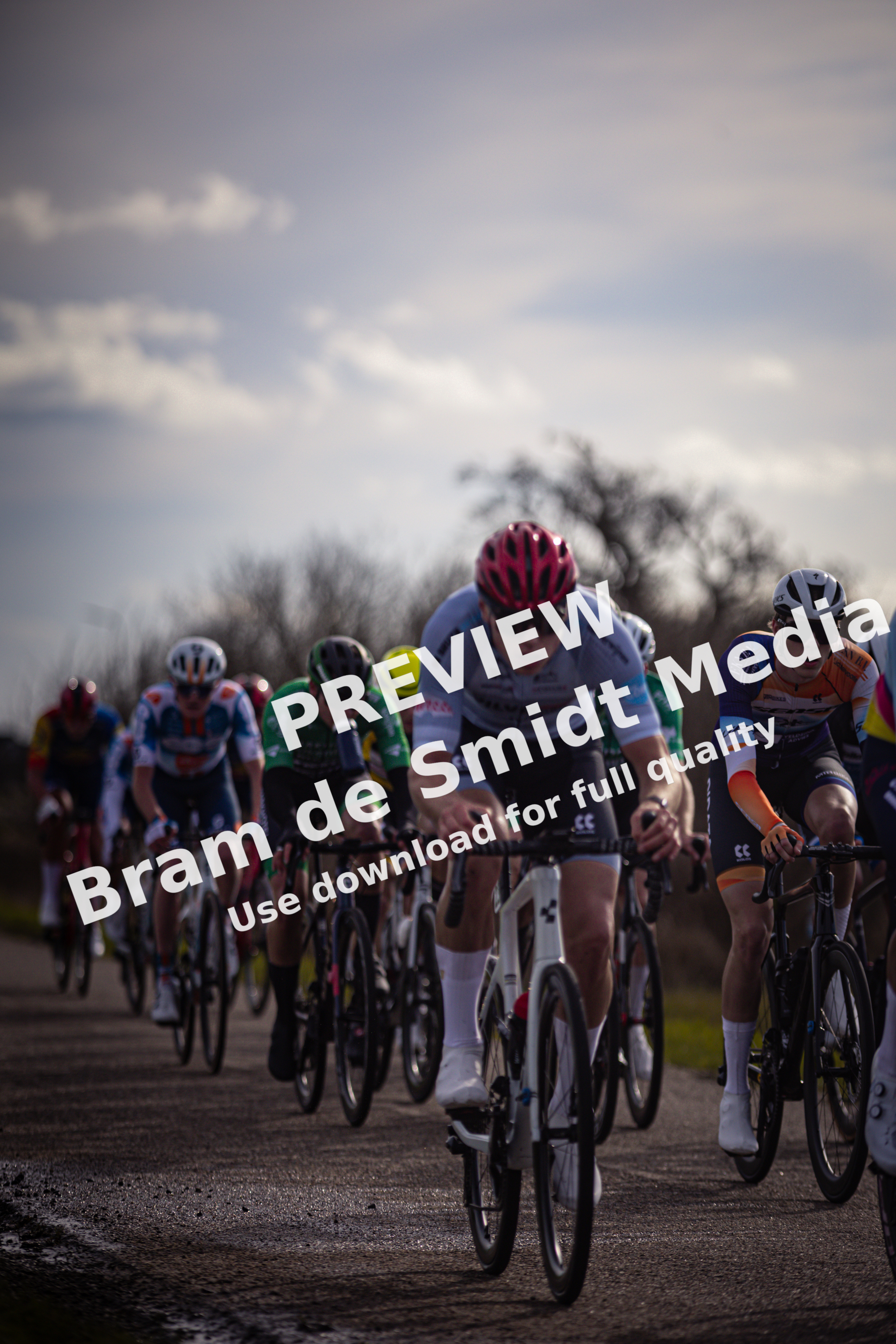 A group of cyclists in a race, one wearing a red helmet and another an orange one.
