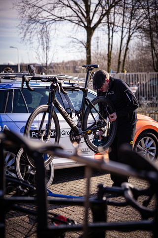 A man prepares a bicycle for a race in Zwolle. He stands next to a car and another bike.