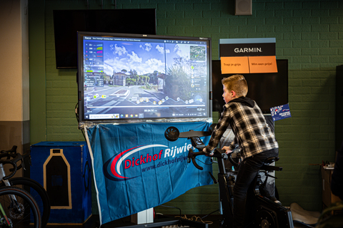 A young boy is on a bike, in front of a screen with information about the Ster van Zwolle.