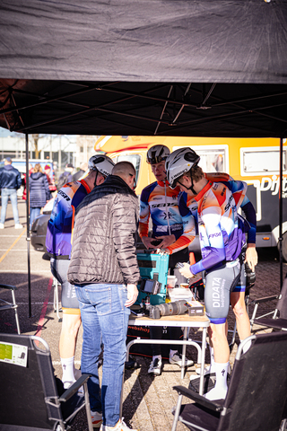 A group of cyclists with one wearing a helmet in front of a sign that says Ster Van Zwolle.