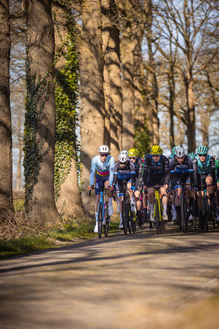 A group of cyclists wearing helmets are riding down a road.