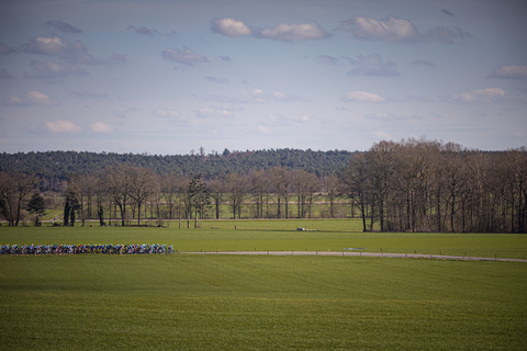 A group of cyclists in a race sponsored by Ster van Zwolle, competing on a track that runs through a green grassy field.