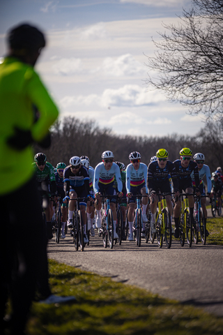 A group of athletes wearing cycling gear are riding their bikes. They have number tags on that say 1 and 3.