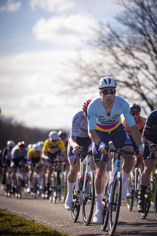 A group of cyclists are racing through a park, one of them is wearing a white helmet that says "STER" on it.