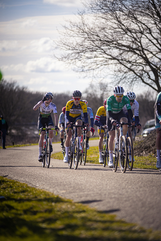 Five cyclists on a road with the rider in the middle wearing a blue, green and white shirt.