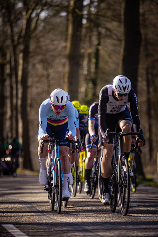 Four men on bikes race down a path. One of them wears the number 25.