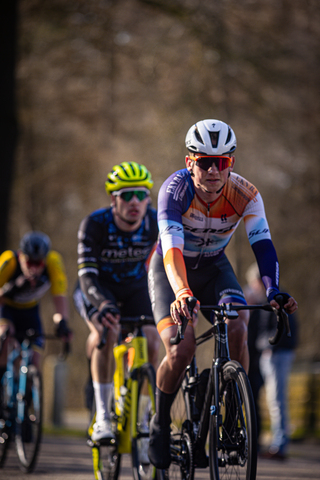 Three men in bicycle races. Two of them wearing a blue and yellow helmet while the one in the middle has a white helmet on.