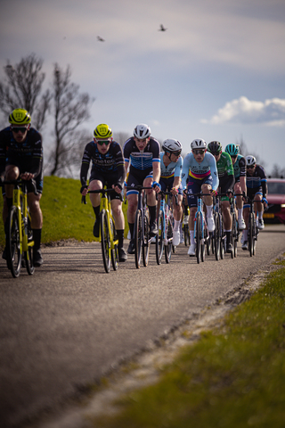 A group of cyclists wearing helmets ride on a road.